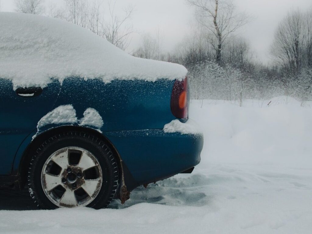 Blå bil täckt av snö i ett kallt, vinterklätt landskap