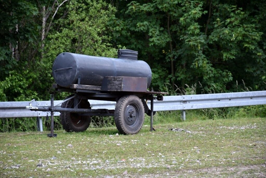 Mörk bränsletank på släpvagn vid en gårdsplan och vägräcke