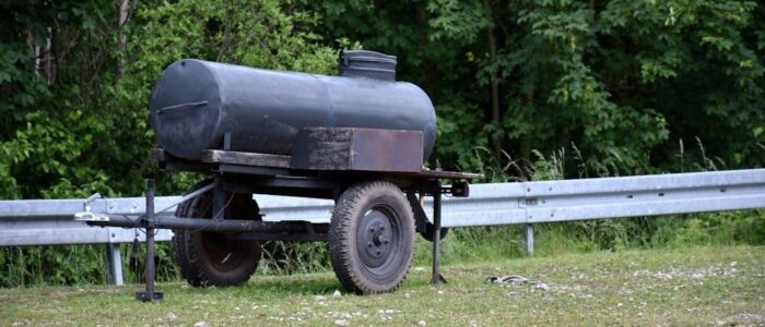 Mörk bränsletank på släpvagn vid en gårdsplan och vägräcke
