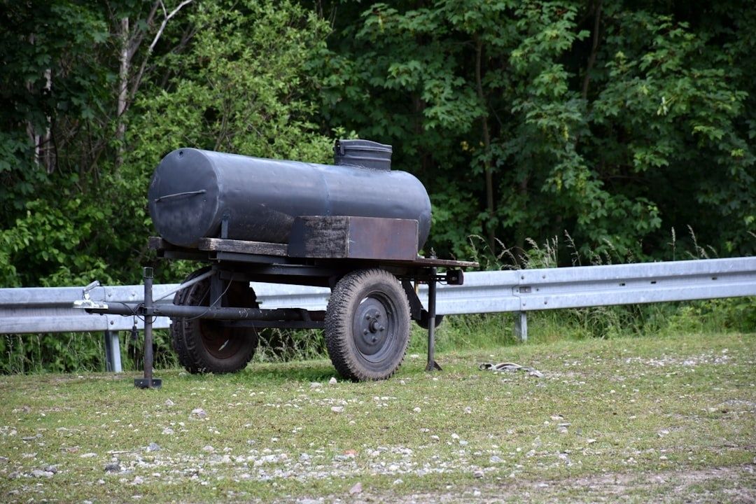 Mörk bränsletank på släpvagn vid en gårdsplan och vägräcke