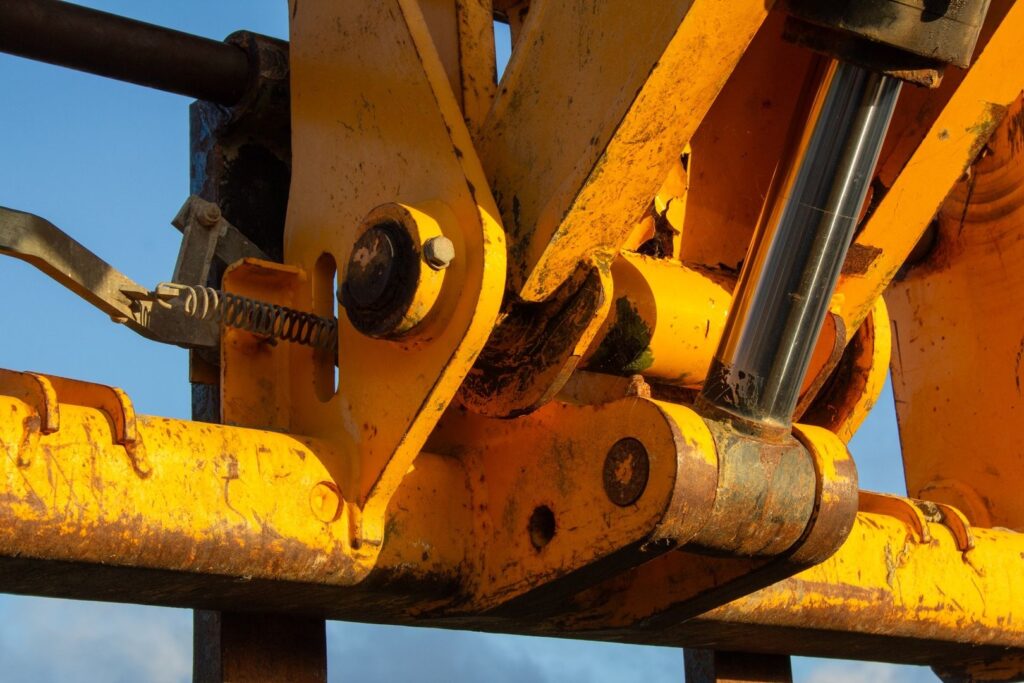 Närbild av sliten gul hydraulcylinder och leder på tung maskin