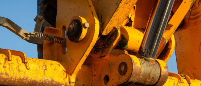 Närbild av sliten gul hydraulcylinder och leder på tung maskin